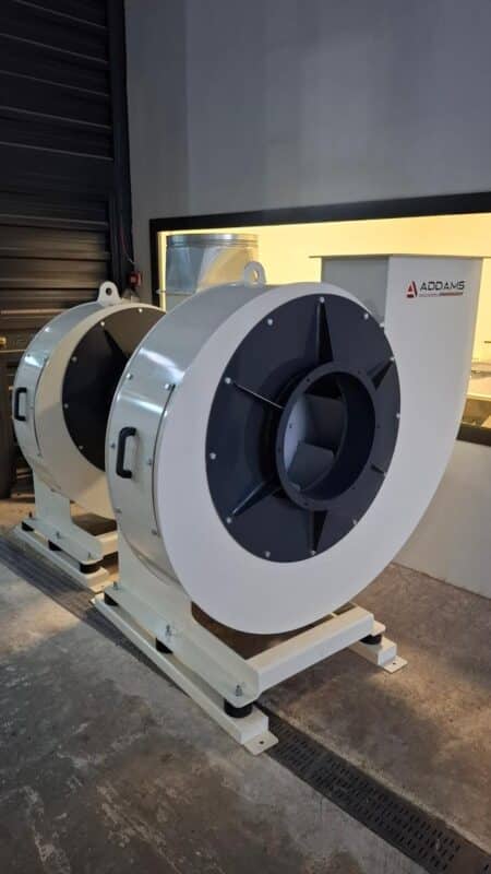 Two ADDAMS centrifugal fans with circular inlet flanges and rectangular discharge outlets in the workshop